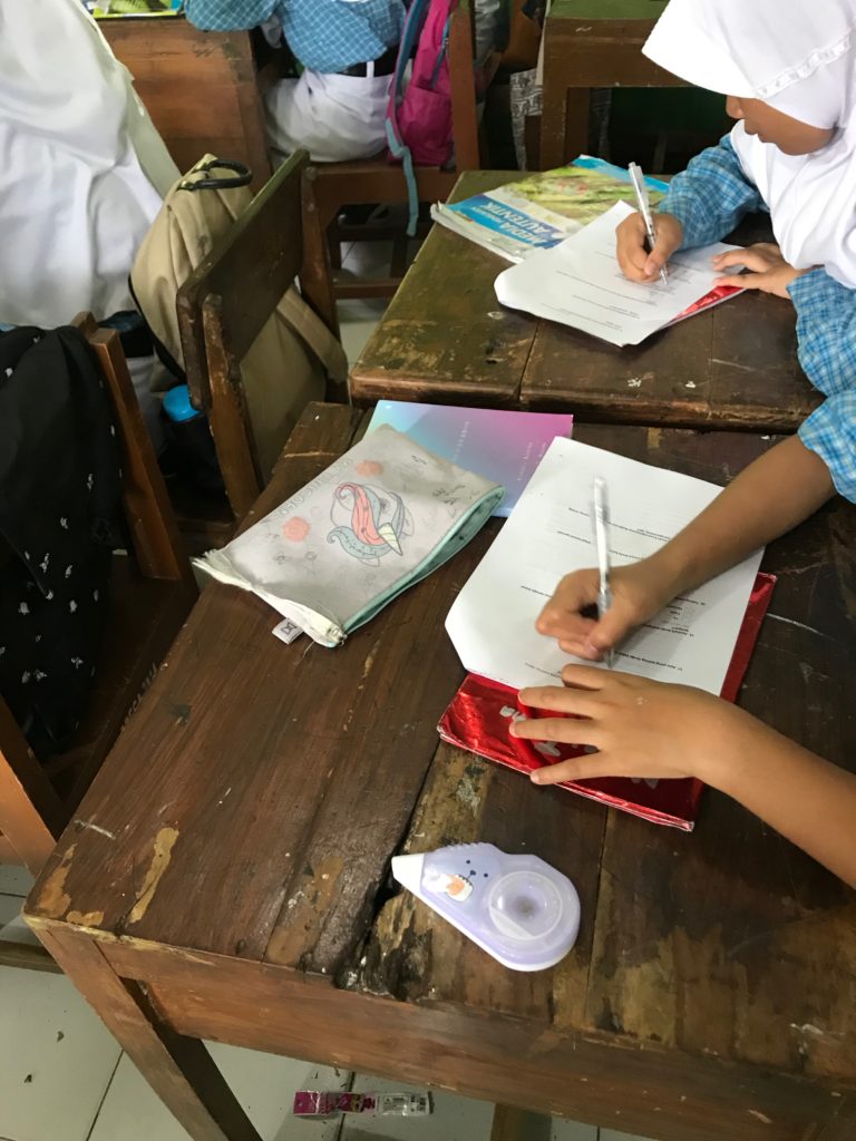 view from above the desk of two students who are writing their answers on our survey